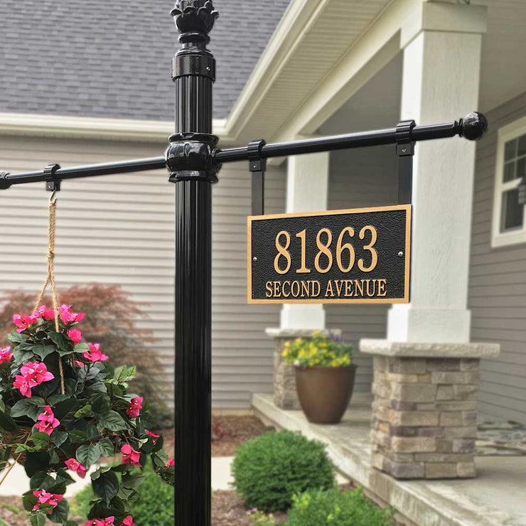 A rectangular cast bronze address plaque hanging on an address plaque post with a pinecone finial and a hanging flower basket