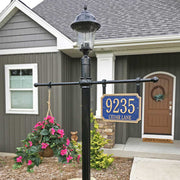 An example address plaque post assembly with a post-top light, a hanging flower basket on one side, and the hanging address plaque on the other side, all in front of a grey house