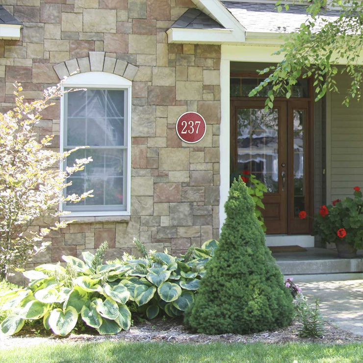 A red round address plaque wall-mounted on a stone-sided home