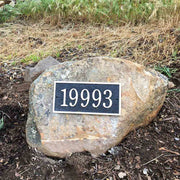 A rectangular bronze address plaque mounted on a large rock / boulder
