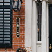 A close-up view of a cast bronze vertical address plaque on a brick home