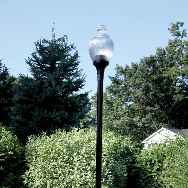 A classic light globe as part of a post top light assembly in front of foliage